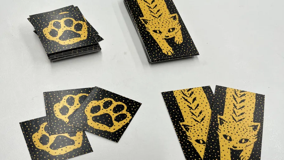 Printed black-and-yellow kitten and footprint cards lying in small piles on a white table.