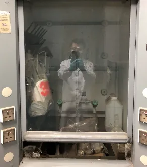 A dusty glass-fronted cabinet; a figure in a white protective suit shows in the glass.