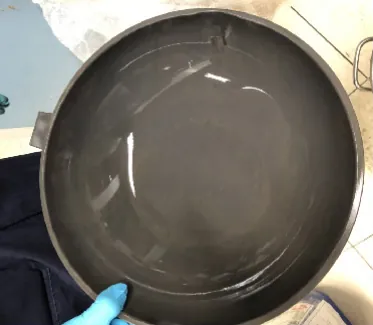A grey sandblasted pan held up by a hand in a blue glove.